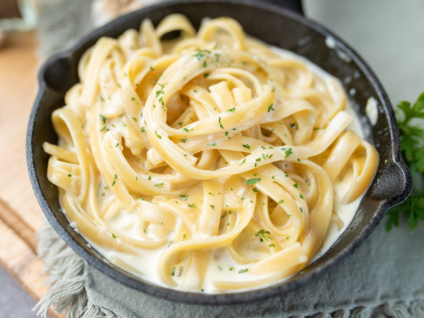 Fettuccine coated in creamy Alfredo sauce in a black skillet