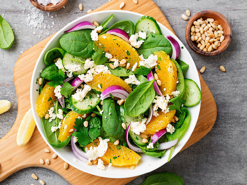 Spinach salad with orange slices, red onion, cucumber, cheese and pine nuts